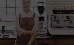 Female barista standing infront of a cafe bench top, where a Brasilia commercial coffee machine and grinder sit
