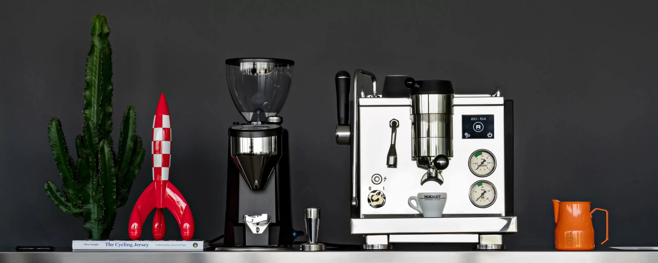 Rocket Espresso home coffee sitting besides a coffee grinder, coffee tamper, milk jug and decorative ornaments