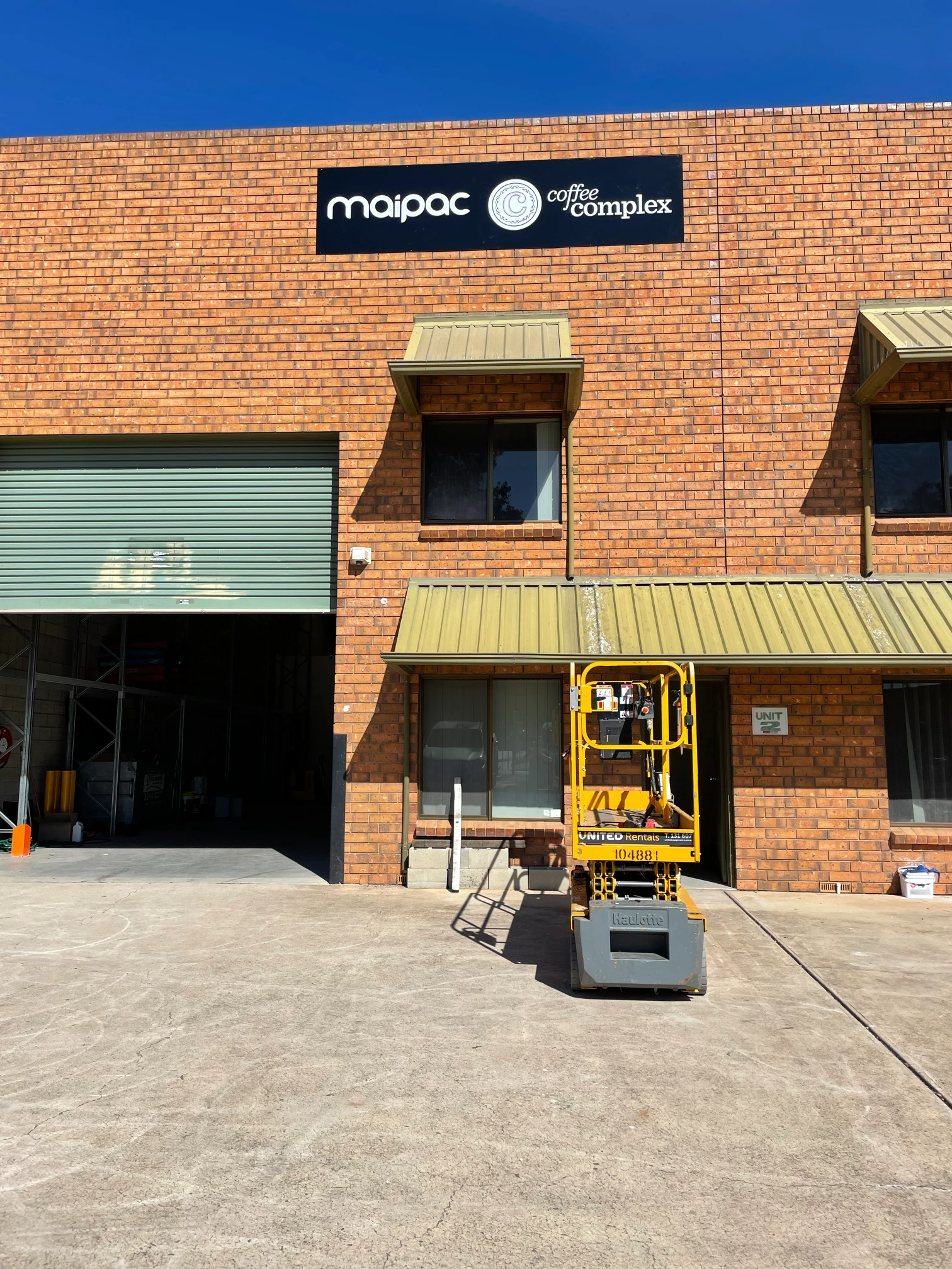 Maipac coffee pod manufacturing Warehouse in Adelaide, with a yellow scissor lift directly infront of the doorway to the warehouse